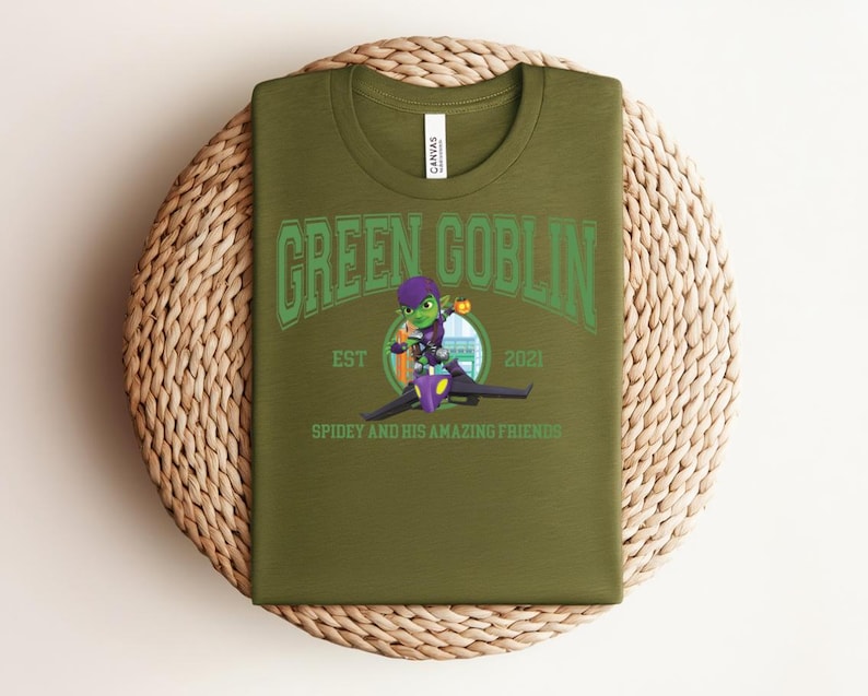 May include: Olive green t-shirt featuring the text "GREEN GOBLIN" in green arched lettering above an illustration of the Green Goblin character riding a glider. The text "EST 2021" and "SPIDEY AND HIS AMAZING FRIENDS" are also visible.