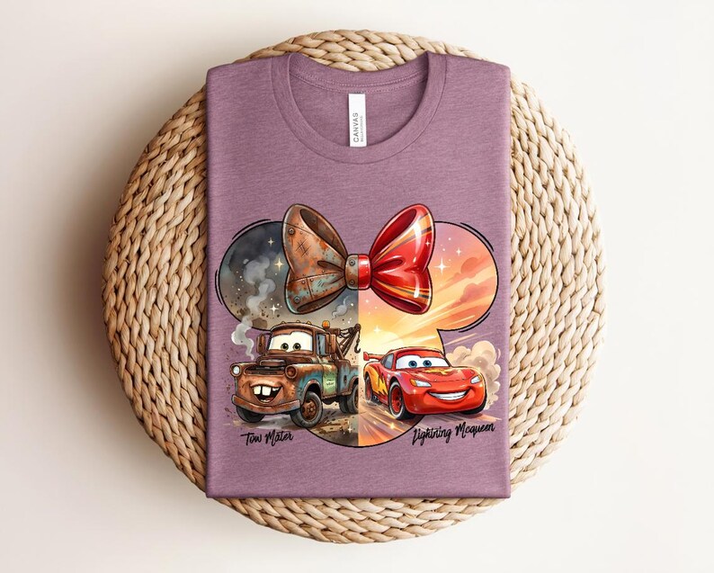 May include: A mauve crew neck t-shirt featuring a graphic of Tow Mater and Lightning McQueen beneath a large red and brown bow. The design includes the text Tow Mater and Lightning McQueen in a script font, set against a circular background.