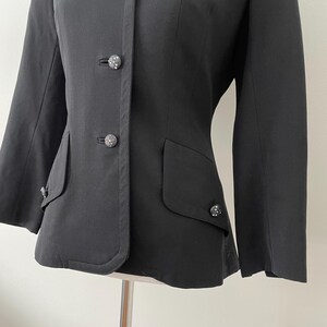 Puede incluir: Una blazer negra con cuello redondo y tres botones decorativos. La blazer tiene dos bolsillos delanteros y mangas largas. Los botones tienen un dise&ntilde;o decorativo y texturizado.