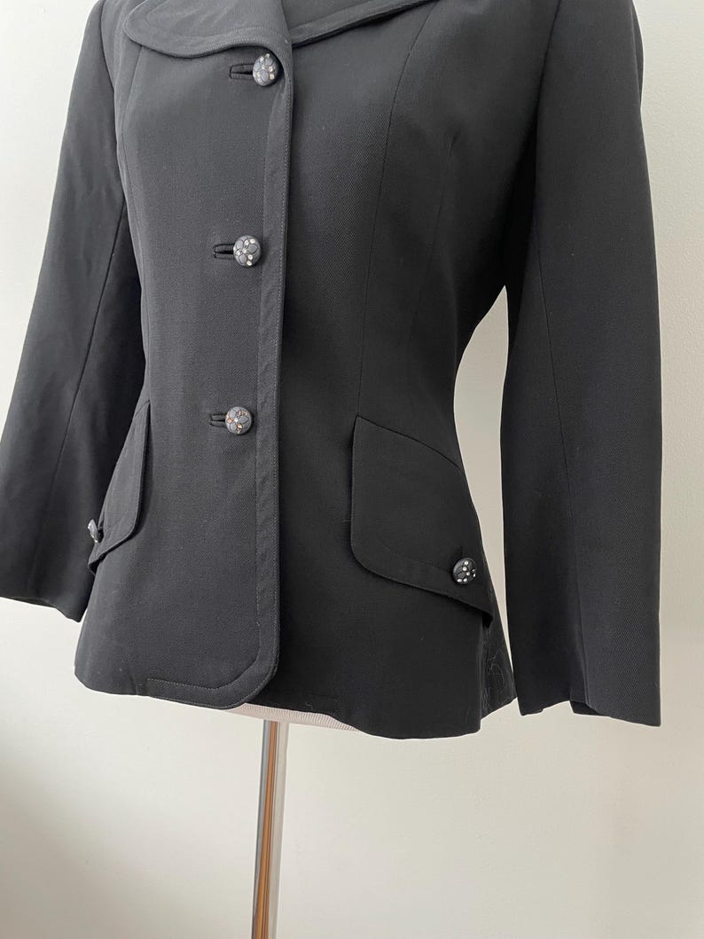 Puede incluir: Una blazer negra con cuello redondo y tres botones decorativos. La blazer tiene dos bolsillos delanteros y mangas largas. Los botones tienen un dise&ntilde;o decorativo y texturizado.