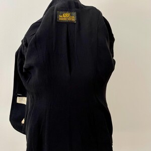 Puede incluir: Un blazer negro con un corte a medida. El interior presenta una etiqueta que dice "THE ADDIS CO. SYRACUSE, NEW YORK". El blazer tiene un dise&ntilde;o cl&aacute;sico, con solapas con muescas y cierre de dos botones. La tela parece ser un material liso y tejido.