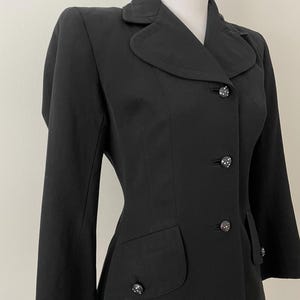 Puede incluir: Un blazer negro con cuello redondo, tres botones decorativos y dos bolsillos delanteros. El blazer se exhibe en un maniqu&iacute; y tiene un corte entallado. Los botones tienen un patr&oacute;n decorativo.