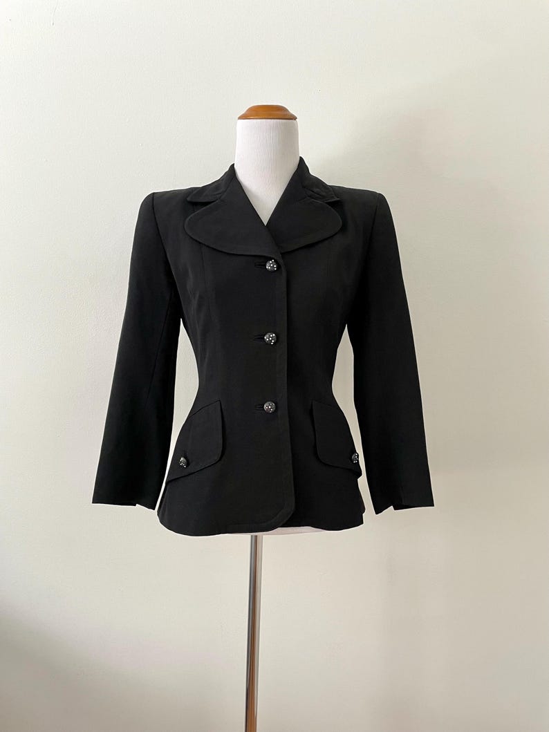 Puede incluir: Una blazer negra con corte entallado, con solapa de muesca y tres botones decorativos. La blazer tiene dos bolsillos delanteros y se muestra en un maniqu&iacute;.
