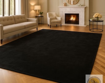 May include: A large, rectangular black rug dominates a living room scene. The rug is placed on a herringbone patterned hardwood floor. The room features a beige sofa, armchair, and a fireplace with a lit fire. A chandelier hangs from the ceiling.