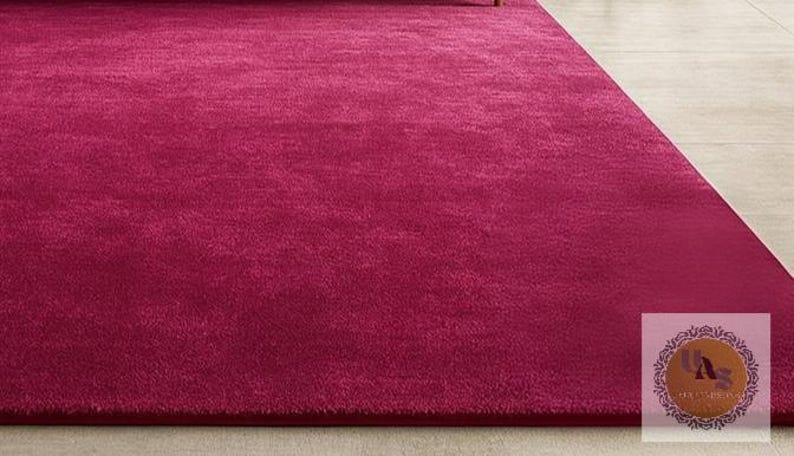 May include: A large, rectangular magenta rug with a soft, plush texture. The rug fills most of the frame, with a small portion of a light-colored floor visible in the background. The rug's color is a deep, vibrant shade of pink.