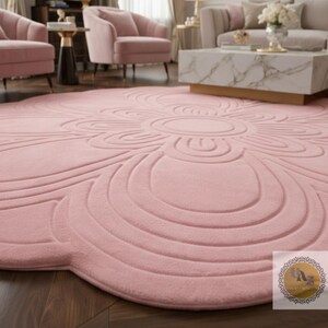 Puede incluir: Una alfombra grande y redonda de color rosa rubor con un dise&ntilde;o floral. La alfombra presenta un motivo circular central rodeado de patrones curvos en capas. La textura afelpada y el color suave crean una est&eacute;tica acogedora y elegante, adecuada para salones o dormitorios.