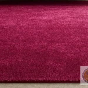 May include: A plush, solid magenta rug. The rug has a soft, textured surface and a deep, rich color. The rug is a rectangular shape and appears to be made of a soft material. This rug is suitable for living rooms and bedrooms.