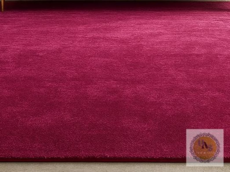 May include: A plush, solid magenta rug. The rug has a soft, textured surface and a deep, rich color. The rug is a rectangular shape and appears to be made of a soft material. This rug is suitable for living rooms and bedrooms.