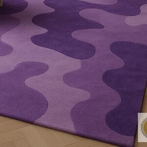 May include: A close-up of a purple area rug with a wavy pattern in varying shades of purple. The rug is made of a soft material and has a plush texture. The design creates a modern and stylish look for any room.