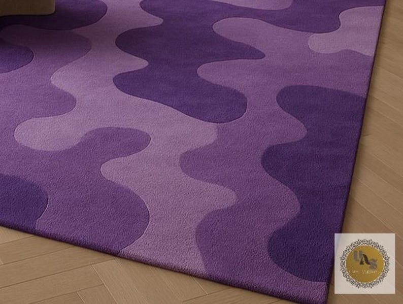 May include: A close-up of a purple area rug with a wavy pattern in varying shades of purple. The rug is made of a soft material and has a plush texture. The design creates a modern and stylish look for any room.