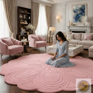 Puede incluir: Una gran alfombra rosa con forma de flor domina el primer plano de un sal&oacute;n. El dise&ntilde;o de la alfombra presenta una serie de l&iacute;neas curvas conc&eacute;ntricas. La habitaci&oacute;n incluye sillones rosas, un sof&aacute; y una mesa de centro de m&aacute;rmol. Una persona est&aacute; sentada en la alfombra.