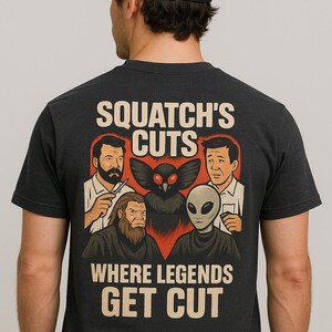 May include: Dark gray t-shirt with the text "SQUATCH'S CUTS WHERE LEGENDS GET CUT". The graphic features cartoon illustrations of a barber, Bigfoot, a Mothman, and an alien. The person in the image is wearing a black baseball cap.