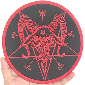 Può includere: Toppa rotonda nera con bordo rosso, raffigurante un pentagramma rosso e un teschio di capra. La toppa ha dettagli ricamati ed è tenuta in una mano.