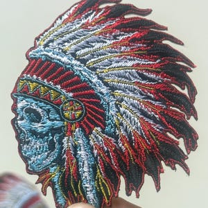 Puede incluir: Parche bordado con un diseño de tocado nativo americano con una calavera. El parche presenta una vibrante paleta de colores rojo, negro, azul, amarillo y blanco. La costura detallada crea una apariencia texturizada, ideal para chaquetas, bolsos u otras prendas.