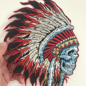 May include: Embroidered patch depicting a Native American headdress and a skull. The patch has a black border with red, white, and blue feathers. The skull is light blue with intricate details, and the headdress has yellow and red accents.