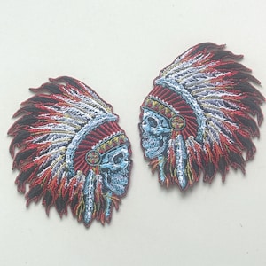 Puede incluir: Dos parches bordados con un diseño de tocado nativo americano con una cara de calavera. Los parches tienen una paleta de colores rojo, blanco, azul y negro. Los parches son simétricos y se enfrentan.