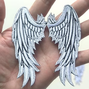 Puede incluir: Parches bordados de alas de ángel blancas con detalles en negro. Las alas presentan un diseño simétrico con patrones de plumas detallados. Ideales para decorar ropa o artículos de tela.