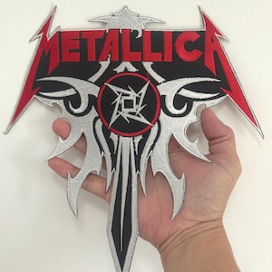 Puede incluir: Parche bordado con el nombre de la banda "METALLICA" en rojo, sobre un diseño negro y plateado. El parche tiene forma de espada estilizada con un emblema central. Los bordes están delineados en rojo.