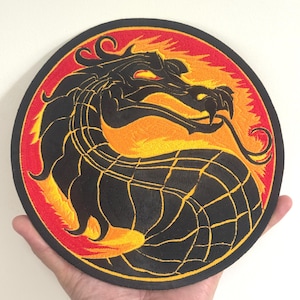 May include: Embroidered patch featuring a black dragon design on a red and orange background. The dragon is in a circular shape with intricate details. The patch has a black border.