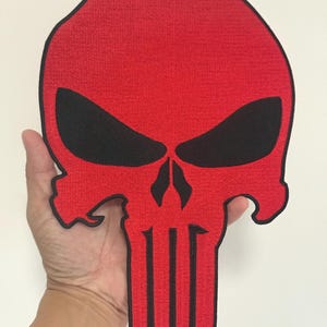 Peut inclure: Un écusson de crâne rouge de grande taille avec des orbites noires et un contour noir. Le patch présente un tissu texturé et un design de crâne distinctif, adapté aux vestes, sacs ou autres vêtements.