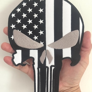 May include: A black and white patch in the shape of a skull. The left side features a design of white stars on a black background, while the right side has white and black vertical stripes. The skull's eyes and nose are tan.