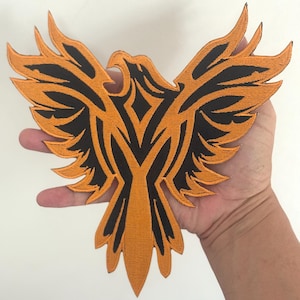 Può includere: Toppa ricamata raffigurante un'aquila arancione e nera con le ali spiegate. La toppa presenta un design dettagliato con una finitura strutturata, adatta per l'applicazione su abbigliamento o accessori. Il disegno dell'aquila è centrato e simmetrico.
