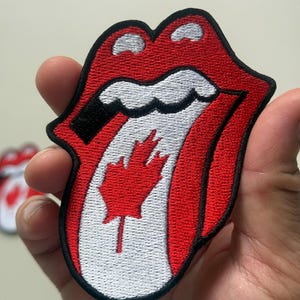 May include: Embroidered patch featuring the iconic red lips logo with a Canadian maple leaf replacing the tongue. The patch has a black border, red lips, white teeth, and a red maple leaf. This patch is suitable for jackets, bags, or other fabric items.