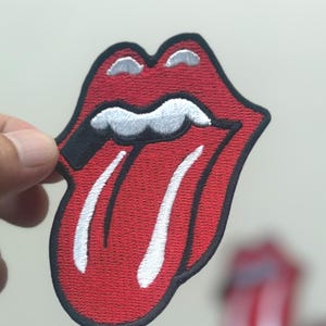 May include: Embroidered patch featuring the iconic red lips and tongue logo. The patch has a black border, white tongue details, and a red lip design. This patch is a popular symbol of rock and roll.
