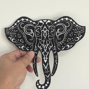May include: A black and white elephant-shaped patch with intricate, decorative patterns. The patch features a detailed design on the ears, head, and trunk. The elephant is held against a white background.