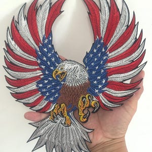 May include: Embroidered patch of an eagle with wings spread wide, showcasing the American flag design. The wings are red, white, and blue. The eagle has a brown body, white head, and yellow talons.