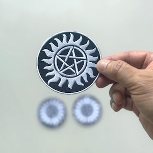 May include: A round, black and white embroidered patch featuring a sunburst design with a five-pointed star in the center. Two additional patches with the same design are visible in the background.