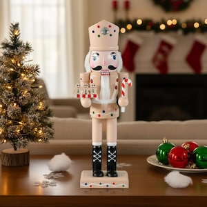 May include: A light tan wooden Christmas nutcracker with a decorative crown and colorful polka dots. The figurine holds a candy cane and a tray of gingerbread men. It stands on a wooden base and wears black boots. The scene is festive.