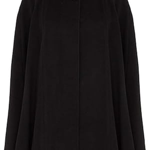 Op de afbeelding: Een zwarte cape met een hoge, ronde kraag en een enkele knoopsluiting. De cape heeft een vloeiend, breed ontwerp, geschikt om in lagen te dragen. De stof lijkt een zacht, effen materiaal te zijn, ideaal voor koeler weer.
