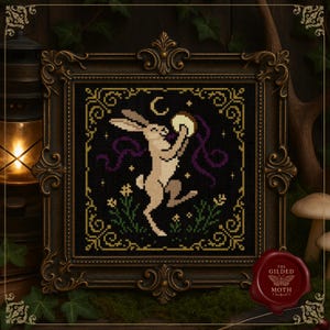 Könnte beinhalten: Kreuzstich-Kunstwerk eines Hasen, der einen Mond hält, mit lila Bändern, vor einem schwarzen Hintergrund mit Sternen und Blumen. Das gerahmte Kunstwerk hat einen goldenen, verzierten Rahmen und ein rotes Siegel.