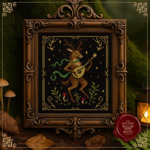 Puede incluir: Arte de punto de cruz en un marco de madera decorativo. La obra presenta un ciervo tocando un laúd, con una bufanda verde, rodeado de plantas y setas sobre un fondo negro. El marco es ornamentado con un acabado marrón oscuro. El logotipo de The Gilded Moth es visible.