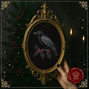 May include: Cross-stitch picture of a crow on a branch with red berries, set against a black background. The artwork is framed in an ornate gold oval frame. The Gilded Moth logo is visible.