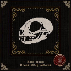 Könnte beinhalten: Kreuzstichmuster eines weißen Katzenschädels auf schwarzem Hintergrund, umrahmt von goldenen Verzierungen. Der Text lautet "Hand drawn Cross stitch patterns" und enthält ein rotes Wachssiegel mit dem Text "The Gilded Moth".