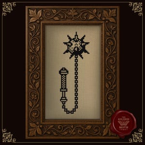 May include: Cross-stitch image of a black flail weapon, presented in an ornate brown wooden frame. The artwork is set against a beige fabric backdrop. A red wax seal with "THE GILDED MOTH" is in the lower right corner.