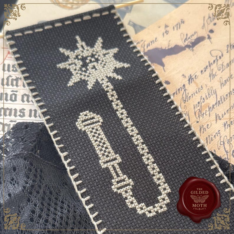 May include: Black and white cross-stitched bookmark featuring a mace design. The bookmark has a white stitched border and is set against a backdrop of aged paper and lace. A red wax seal with a butterfly is in the lower right corner.