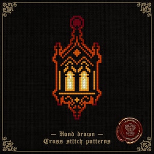 Op de afbeelding: Kruissteekpatroon van een gestileerde lantaarn in tinten oranje, rood en geel tegen een zwarte achtergrond. Het ontwerp bevat twee verlichte ramen en sierlijke details. Tekst luidt "Hand drawn Cross stitch patterns". Een zegel met "The Gilded Moth" staat rechtsonder.