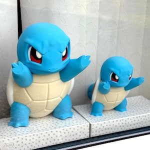 May include: Two blue and cream-coloured turtle-like figures with large eyes and pointed ears, posed with arms extended forward. The figures feature a smooth, matte finish and are displayed on rectangular boxes with a light grey dotted pattern.