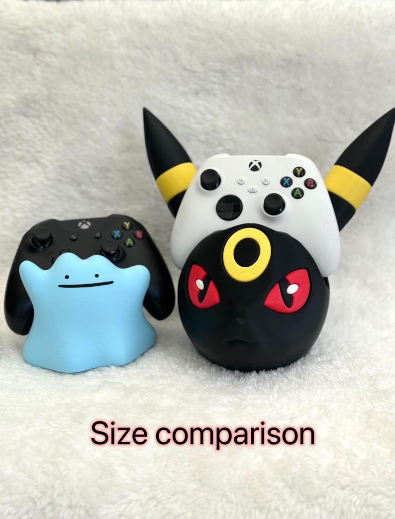 May include: A light blue Ditto-shaped controller stand next to a black Xbox controller, and a black and yellow Umbreon-shaped controller stand holding a white Xbox controller. The text "Size comparison" is visible at the bottom of the image.