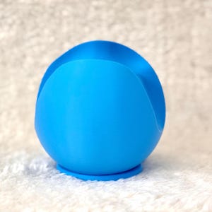 K&ouml;nnte beinhalten: Ein leuchtend blaues, kugelf&ouml;rmiges Objekt mit einer geschwungenen Vertiefung oben. Das Objekt hat eine glatte Textur und steht auf einem kleinen, kreisf&ouml;rmigen Sockel. Das Design ist modern und minimalistisch.