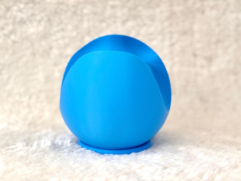 K&ouml;nnte beinhalten: Ein leuchtend blaues, kugelf&ouml;rmiges Objekt mit einer geschwungenen Vertiefung oben. Das Objekt hat eine glatte Textur und steht auf einem kleinen, kreisf&ouml;rmigen Sockel. Das Design ist modern und minimalistisch.