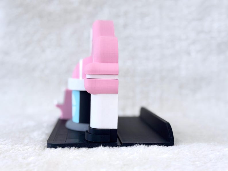May include: A 3D printed display stand featuring a pink and white structure with a light blue accent, mounted on a black rectangular base. The object has a layered, matte finish with a distinct side profile showing a vertical design.