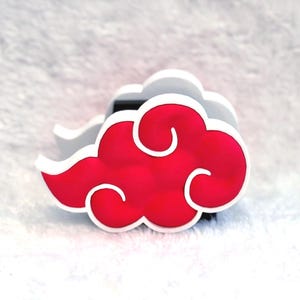 May include: A three-dimensional cloud-shaped object featuring a vibrant red center with rounded, swirling edges outlined in a thick white border. The design has a layered appearance with a black base visible behind the red cloud shape.