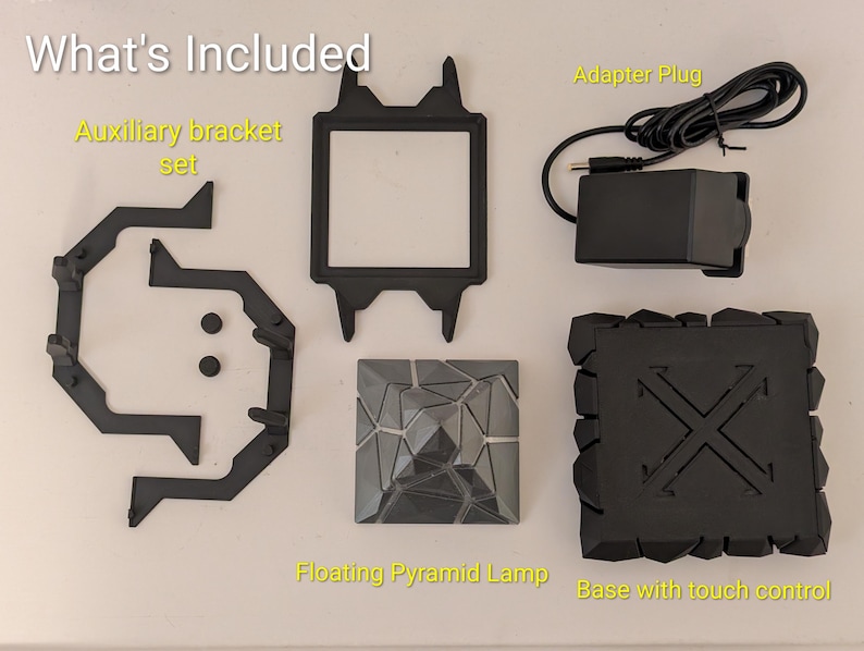 May include: A collection of black components for a floating pyramid lamp, including an auxiliary bracket set, a square frame, an adapter plug, a pyramid-shaped lamp, and a base with touch control. The text "What's Included" is at the top.