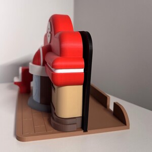 May include: A 3D-printed model of a retro diner, featuring a red roof and seating area, a tan facade, and a brown base. The model has a black trim and white accents, with a light blue section. The diner model is a toy or decorative item.