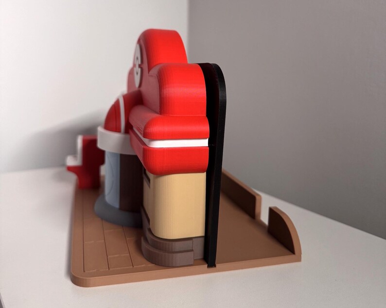 May include: A 3D-printed model of a retro diner, featuring a red roof and seating area, a tan facade, and a brown base. The model has a black trim and white accents, with a light blue section. The diner model is a toy or decorative item.
