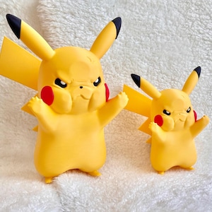 May include: Two yellow Pikachu figures with angry expressions, black-tipped ears, and red cheek circles. The figures feature a lightning bolt-shaped tail and are standing in a pose with arms raised, showcasing a larger and a smaller version side by side.